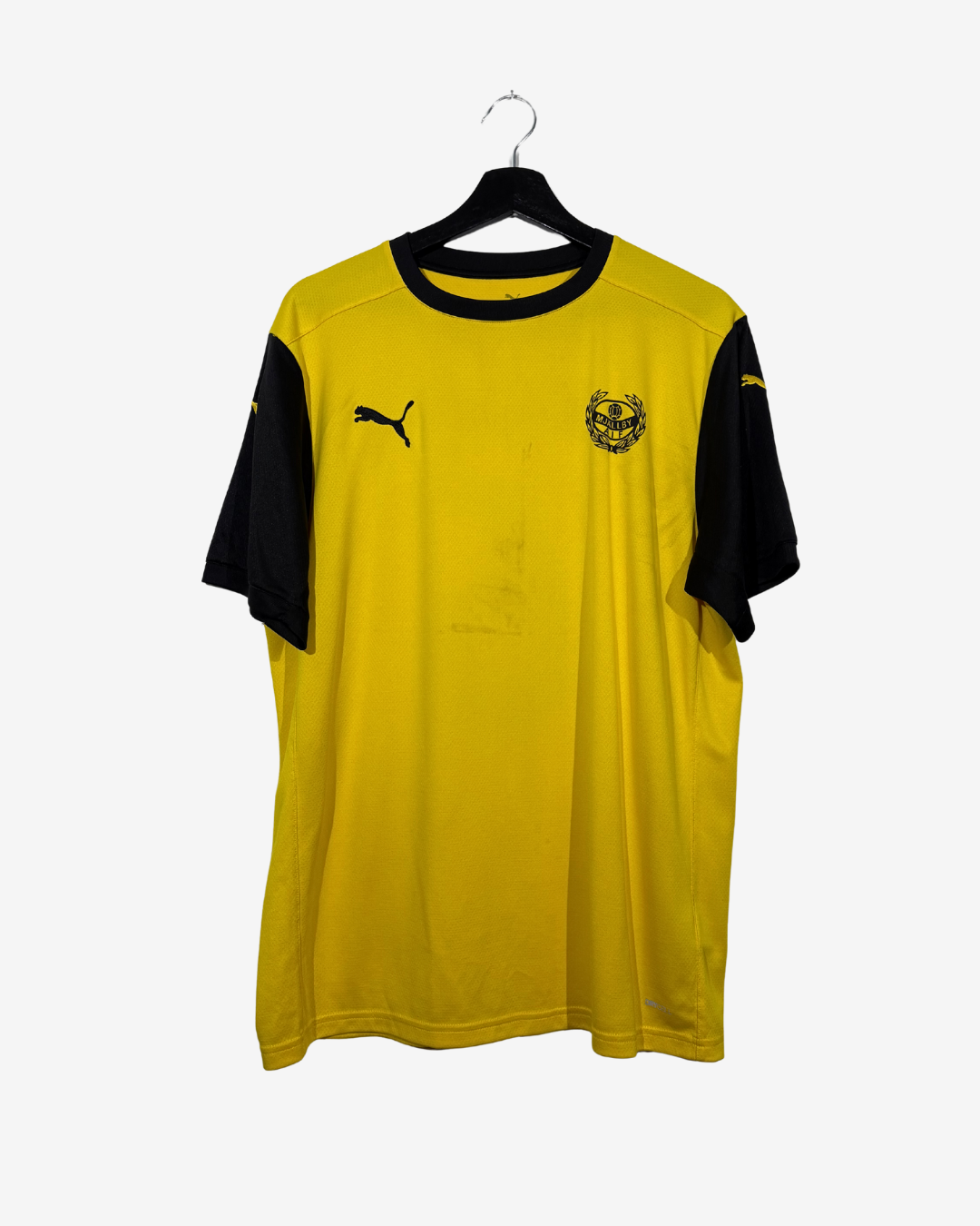 A yellow and black Puma soccer jersey hanging on a black hanger against a light gray background. The jersey features a yellow body, black sleeves, a black collar, a black Puma logo on the right chest, and a gold crest on the left chest.