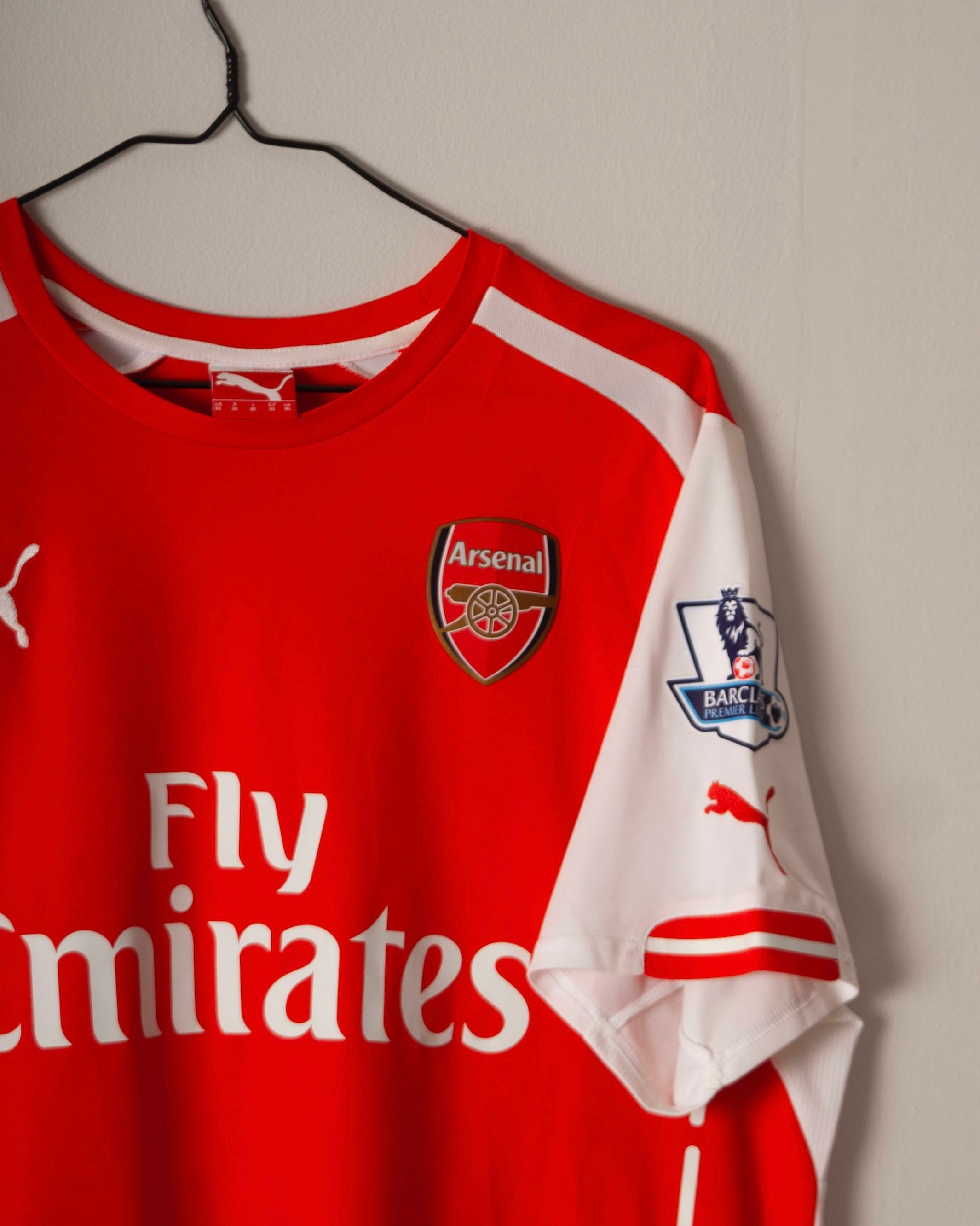 Red Arsenal sports jersey with club logo and sponsor text on a hanger against a plain background