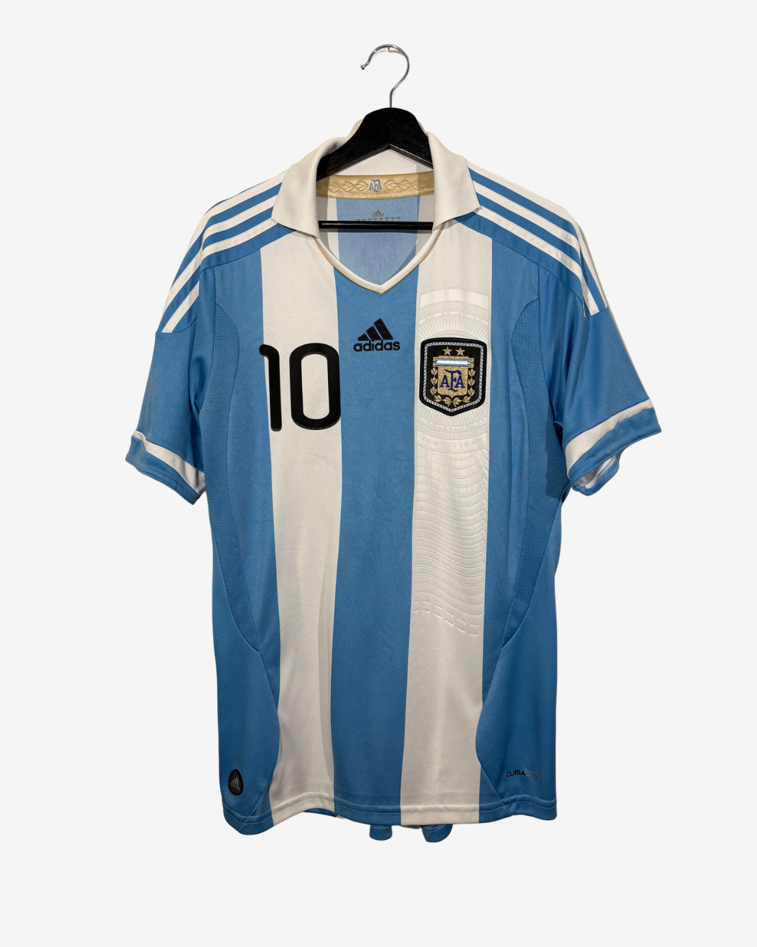 An Argentina national football team home jersey by Adidas, featuring light blue and white vertical stripes, the number 10 on the chest, and the AFA crest, hanging on a black hanger against a light gray background.