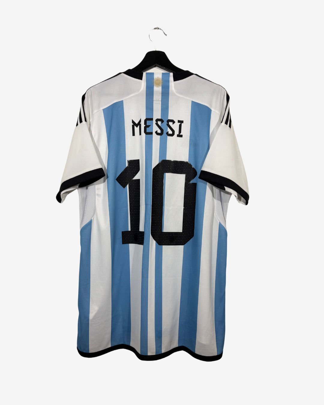 The back of an Argentina national football team home jersey featuring light blue and white vertical stripes, with 'MESSI' and the number '10' printed in black. The jersey is displayed on a black hanger against a light gray background.