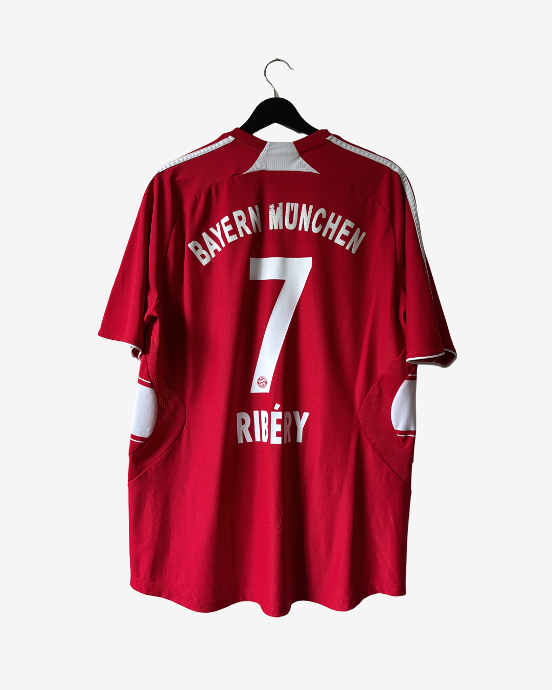 A red Bayern Munich soccer jersey with the name RIBERY and number 7 printed on the back, hanging on a black hanger against a light gray background.