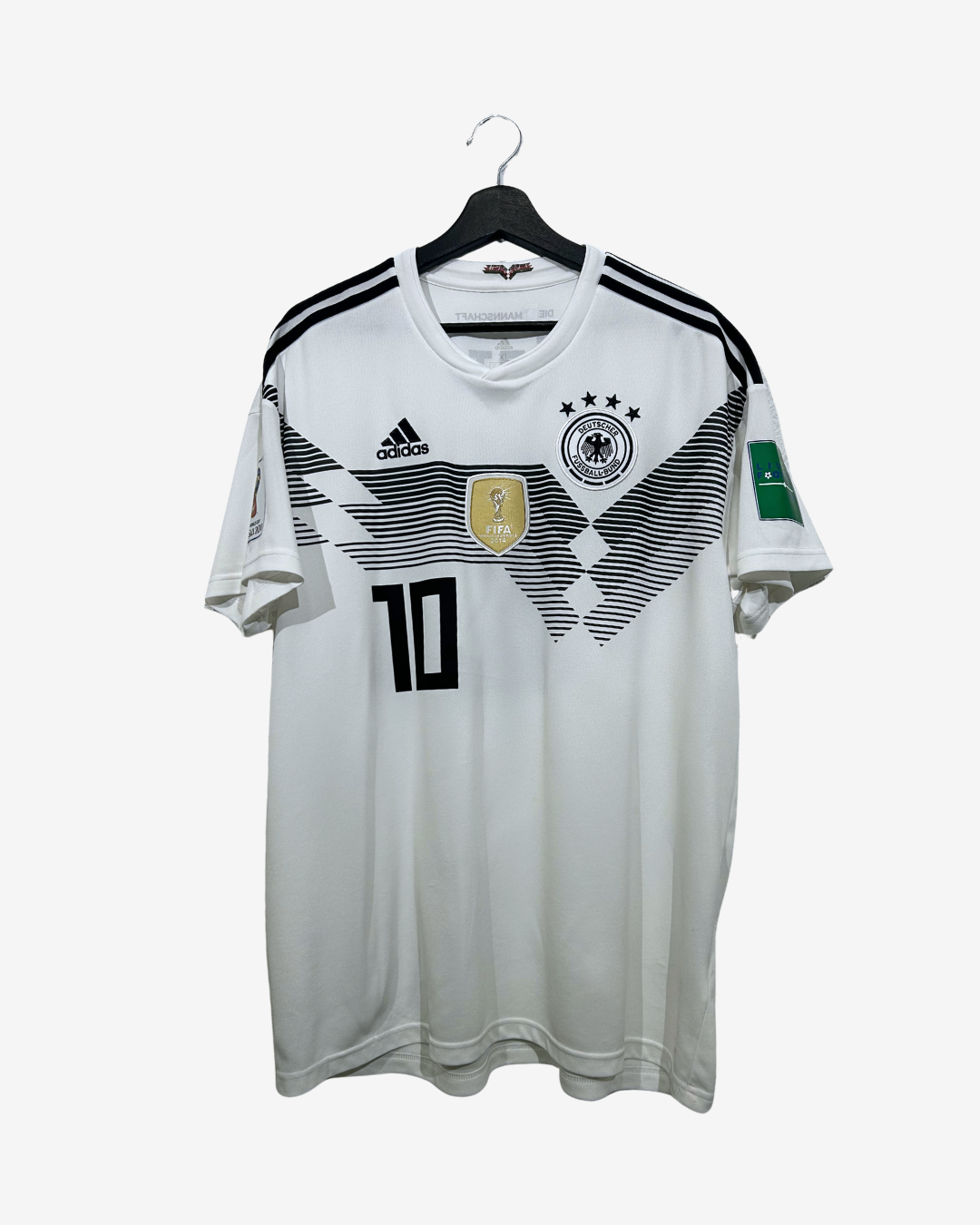 A white Adidas Germany national football team jersey with black and gray graphic patterns, featuring the number 10 on the front, hanging on a black hanger against a light gray background.