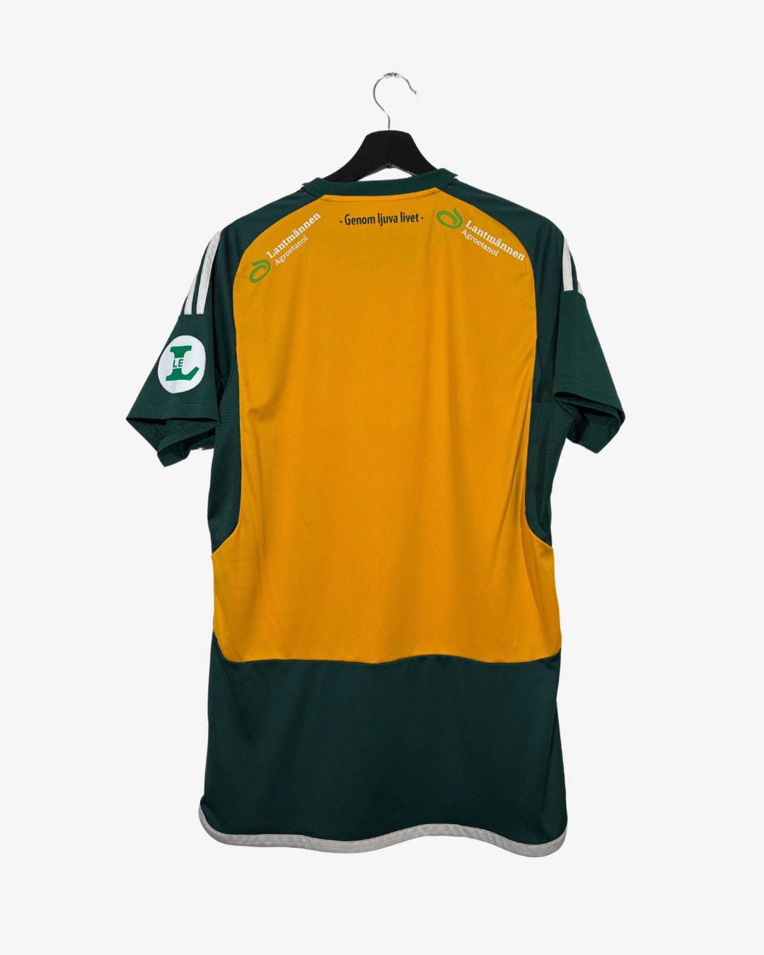 A short-sleeve sports jersey shown from the back, hanging on a black hanger against a light gray background. The jersey has a large mustard yellow center panel with dark green shoulders, sleeves, and lower body, plus white shoulder stripes and printed sponsor text across the upper back.