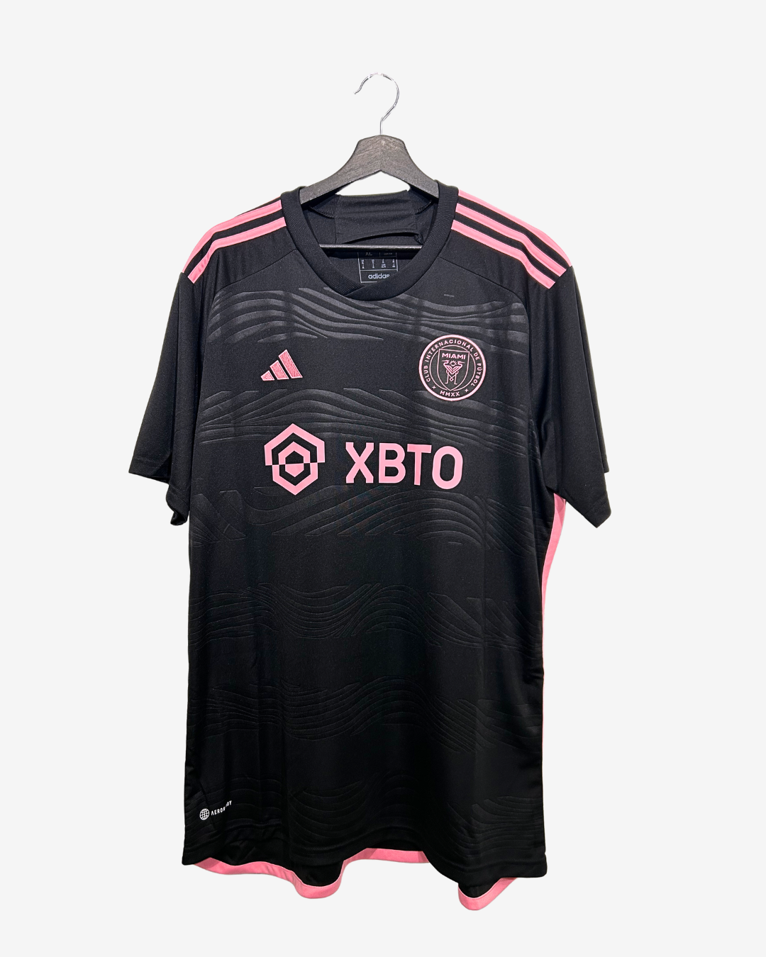 Black sports jersey with pink accents and branding on a hanger against a white background