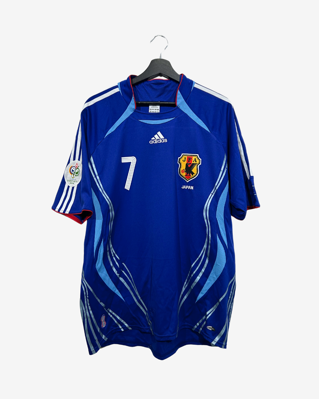 A blue Adidas Japan national football team jersey with the number 7, hanging on a black hanger against a light gray background.