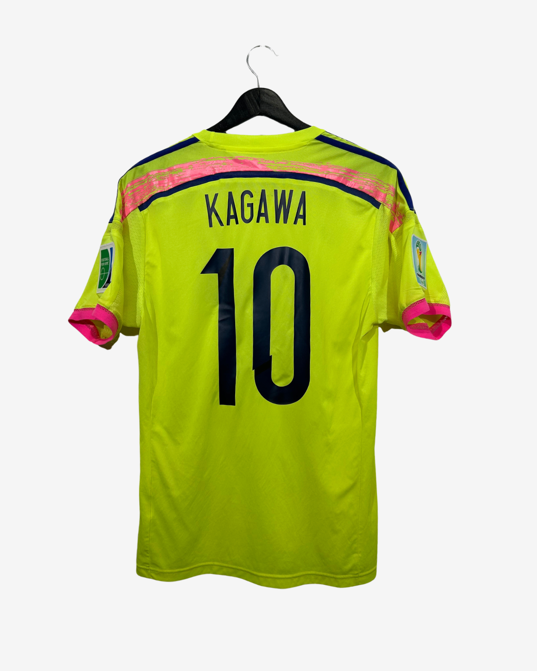 A bright neon yellow-green soccer jersey hanging on a black hanger against a light gray background. The back of the shirt features the name 'KAGAWA' and the number '10' in black, with pink and navy blue accents on the shoulders and sleeve cuffs.