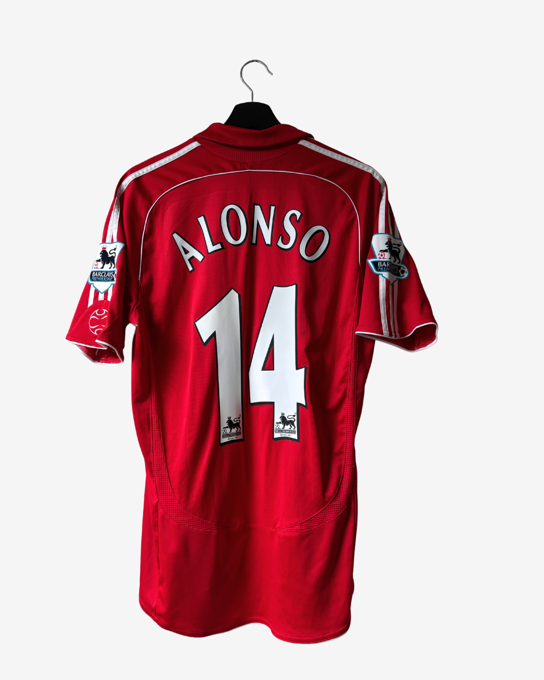 A red short-sleeve soccer jersey hanging on a black hanger against a light gray background. The back of the jersey features the name 'ALONSO' and number '14' in white with black outlines, along with Premier League patches on the sleeves.