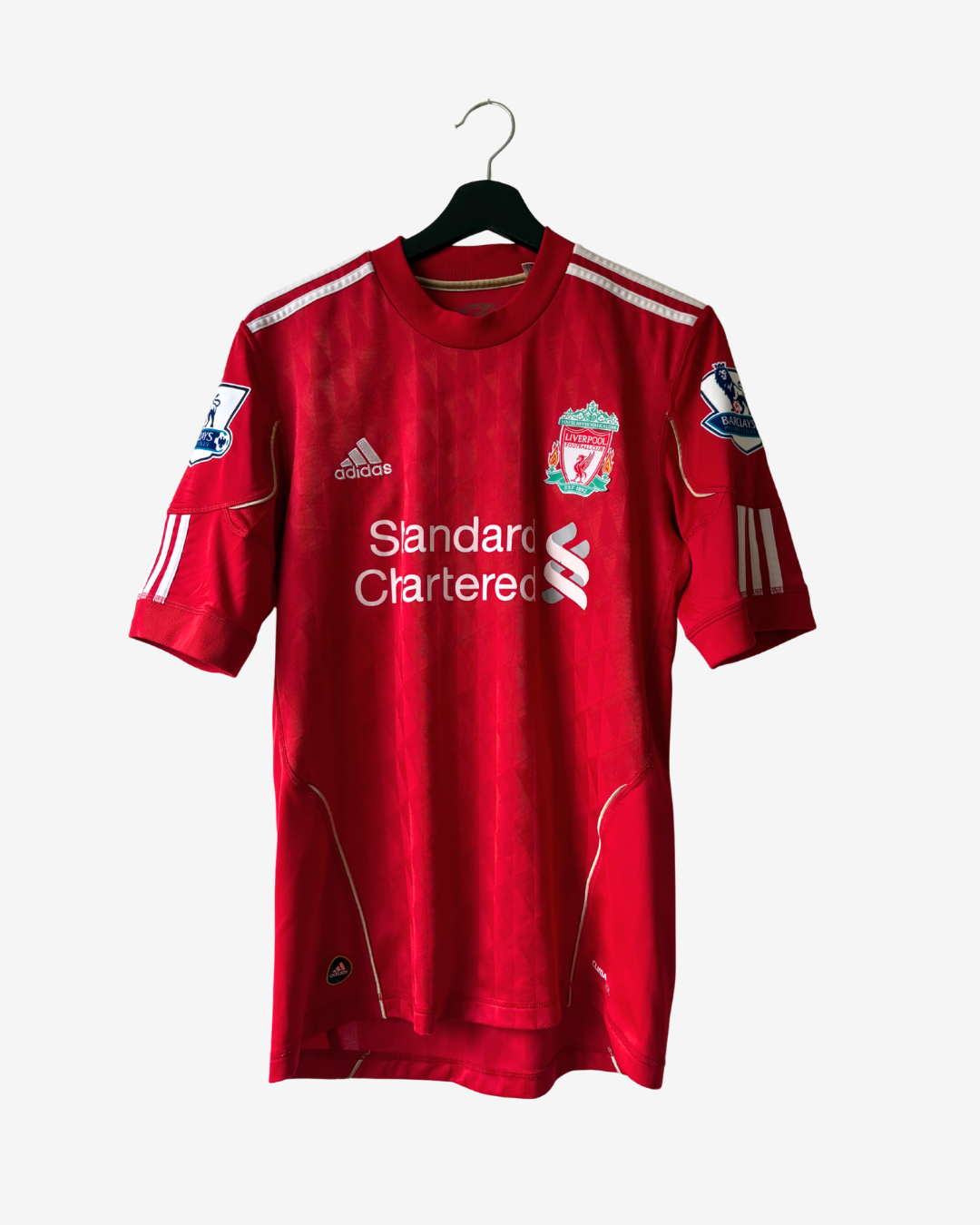 A red Adidas Liverpool football jersey with white sponsor logos and sleeve stripes, hanging on a black hanger against a light gray background.