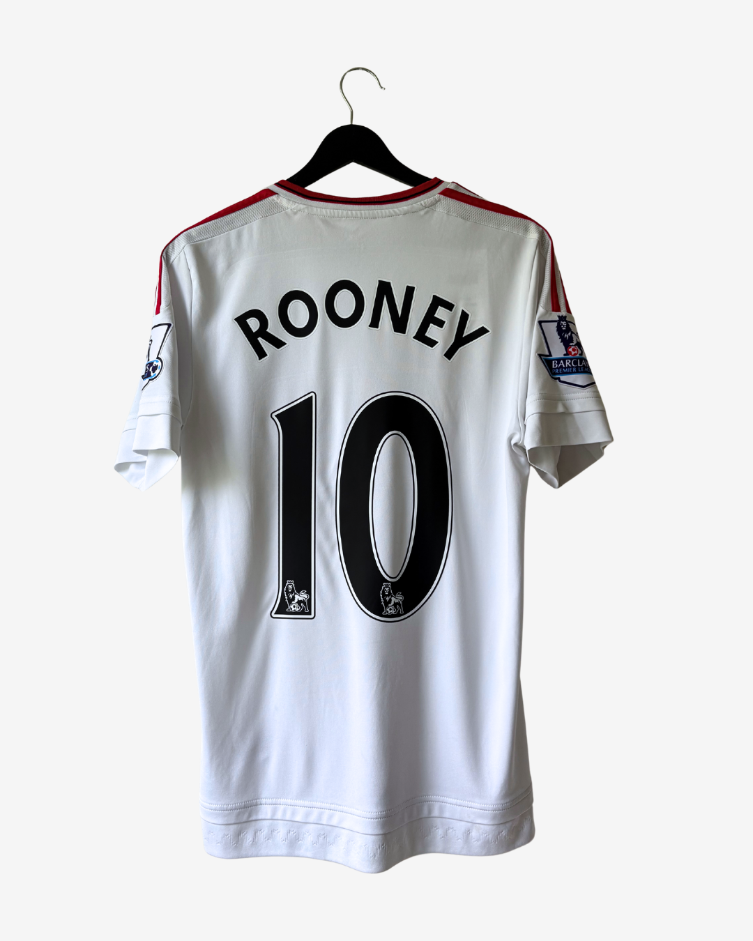 A white Manchester United soccer jersey with 'ROONEY' and the number '10' printed on the back, hanging on a black hanger against a light gray background.