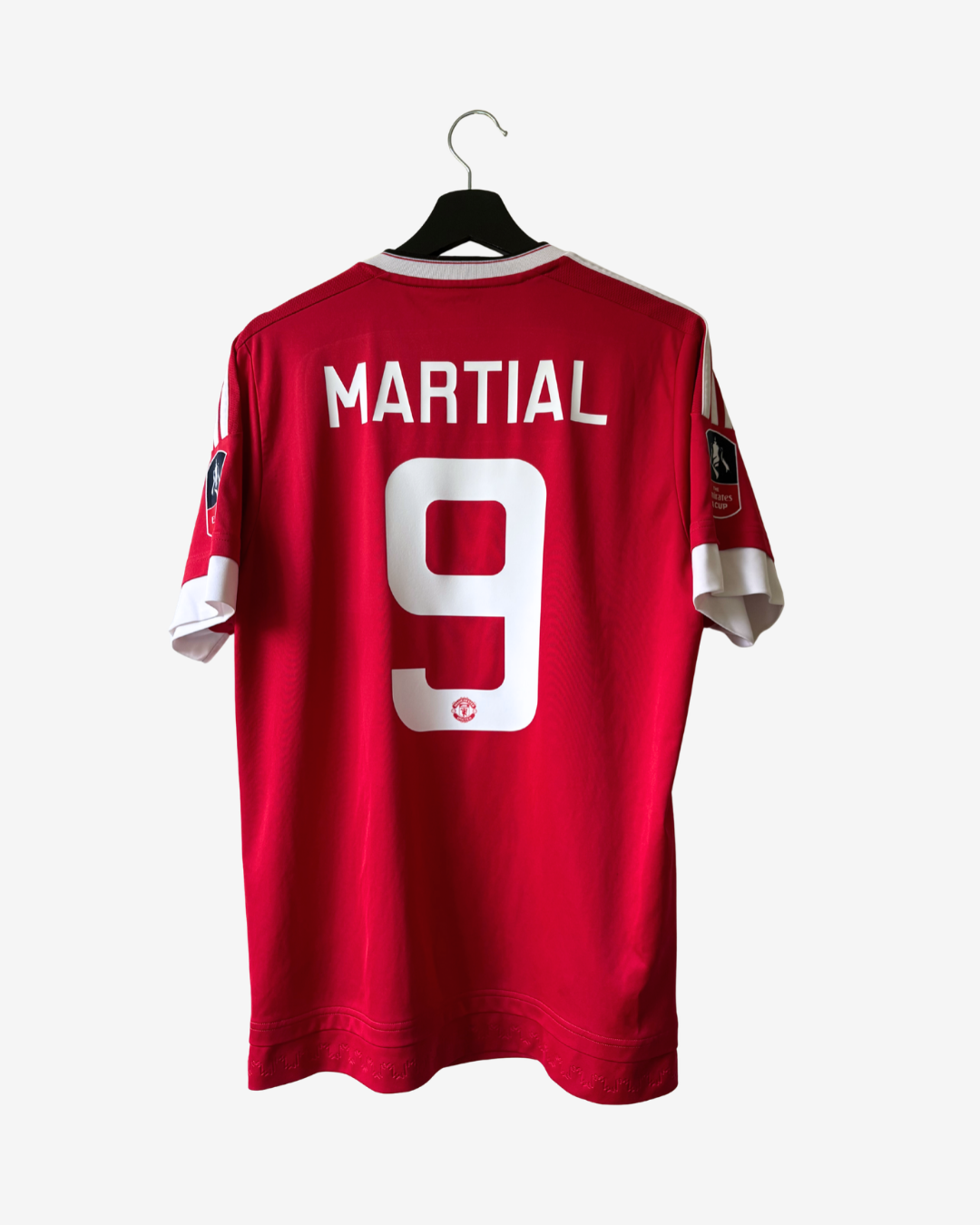 A red short-sleeve football jersey hanging on a black hanger against a light gray background. The back of the shirt shows the name 'MARTIAL' and the number '9' in white, with a small Manchester United crest below the number.