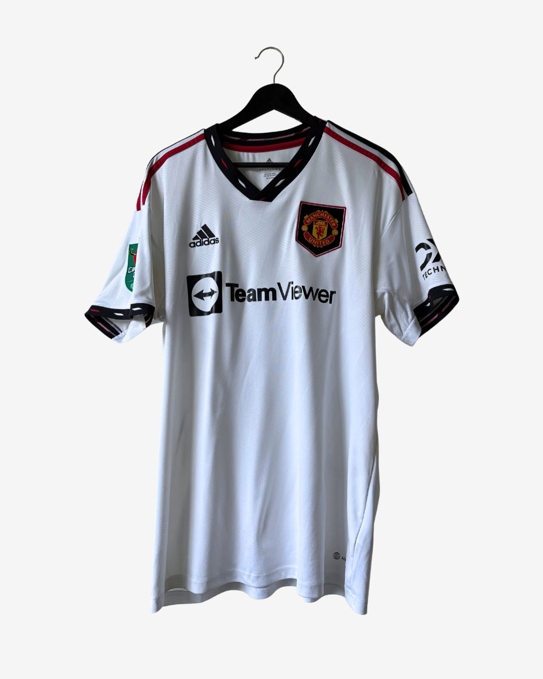 A white Adidas Manchester United soccer jersey with black and red trim, hanging on a black hanger against a light gray background. The jersey features the Manchester United crest on the left chest, the black adidas logo on the right chest, and 'TeamViewer' printed across the center.
