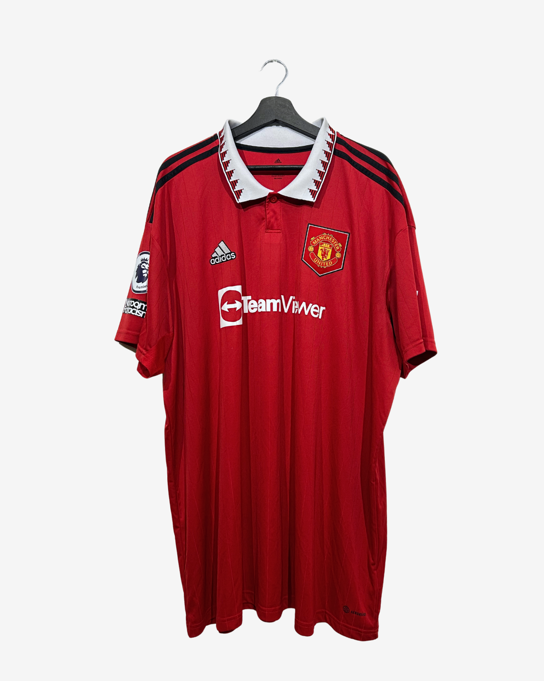 A red Manchester United football jersey by Adidas, featuring the TeamViewer sponsor logo and club crest, hanging on a black hanger against a light gray background.
