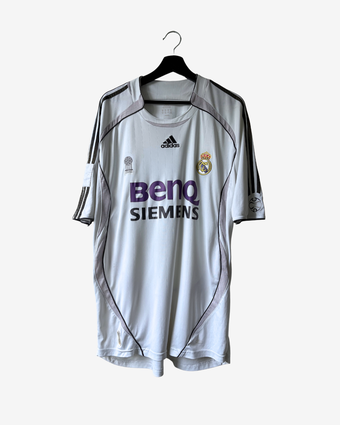 A white Real Madrid soccer jersey by Adidas, featuring the purple Siemens and BenQ sponsor logos, hanging on a black hanger against a light gray background.
