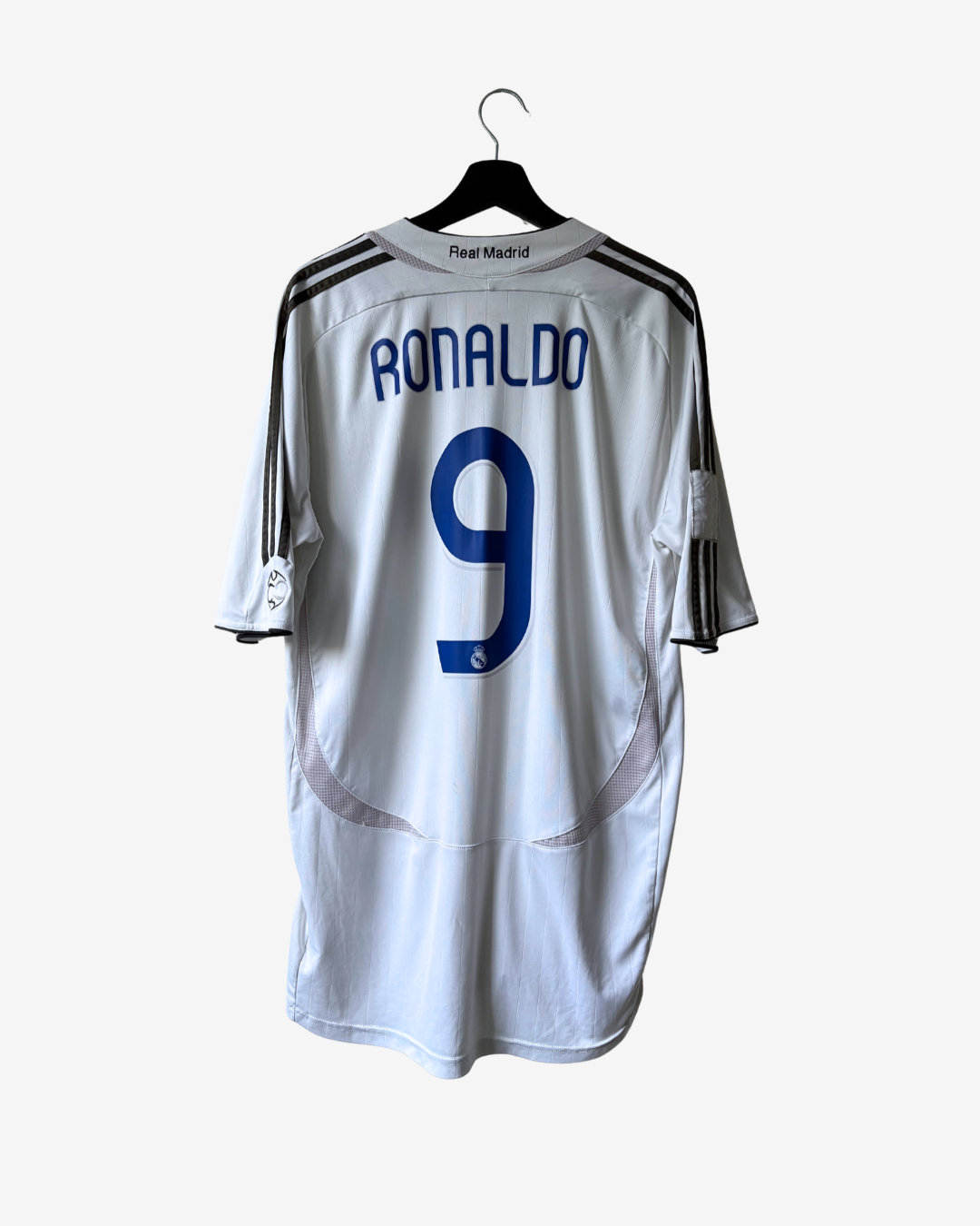 White Real Madrid soccer jersey with 'RONALDO' and number '9' printed in blue on the back, hanging on a black hanger against a light gray background.