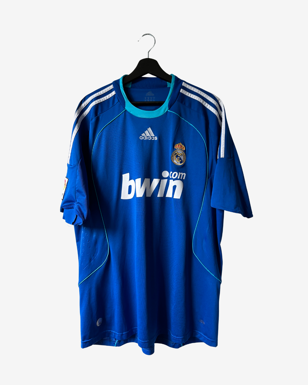 A blue Real Madrid soccer jersey by adidas, featuring the white bwin.com sponsor logo on the front, hanging on a black hanger against a light gray background.