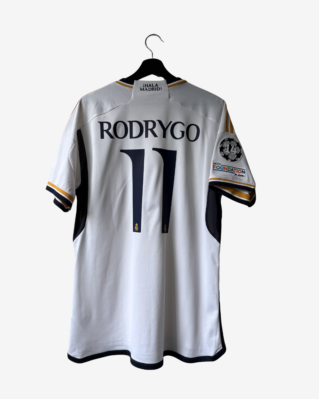 A white Real Madrid jersey with 'RODRYGO' and the number '11' printed on the back, hanging on a black hanger against a light gray background.