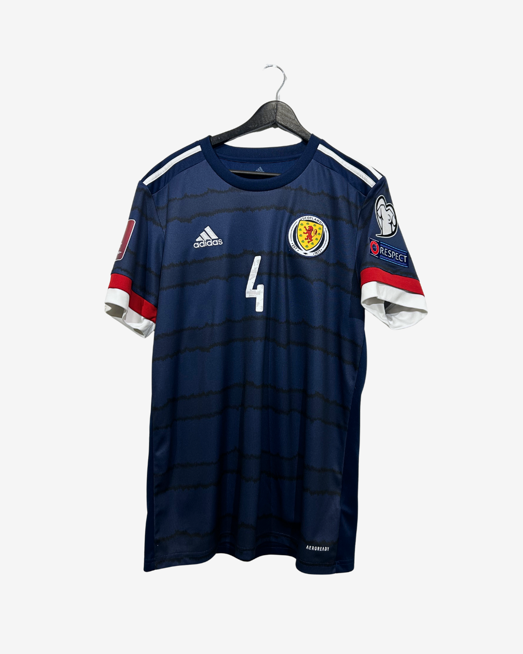 A dark navy blue Scotland national football team jersey with horizontal black stripes, featuring the number 4 on the front, the white Adidas logo, and the Scotland crest. The jersey is shown hanging on a black hanger against a light gray background.