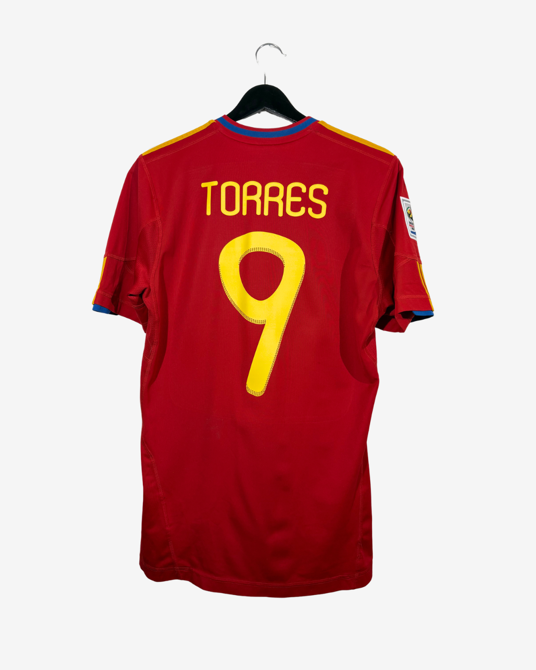 A red short-sleeve soccer jersey hanging on a black hanger against a light gray background. The back of the shirt features the name 'TORRES' and the number '9' in yellow, with blue and yellow trim at the collar and sleeve cuffs.
