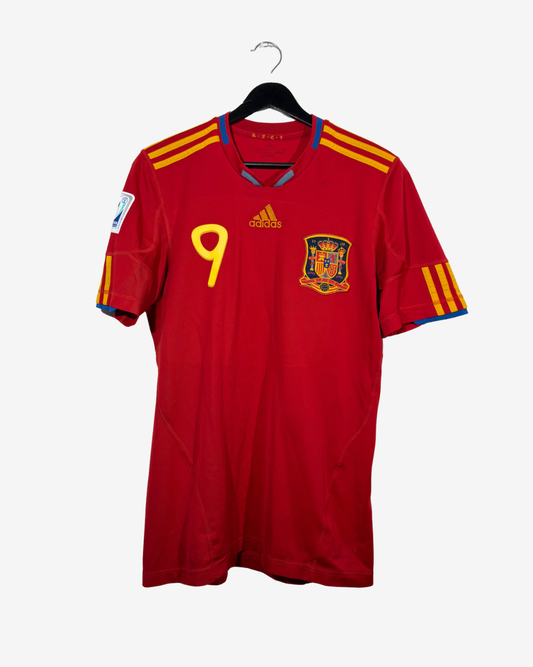 A red Spain national football team jersey with yellow and blue accents, featuring the number 9 on the chest, the Adidas logo, and the Spain crest, hanging on a black hanger against a light gray background.