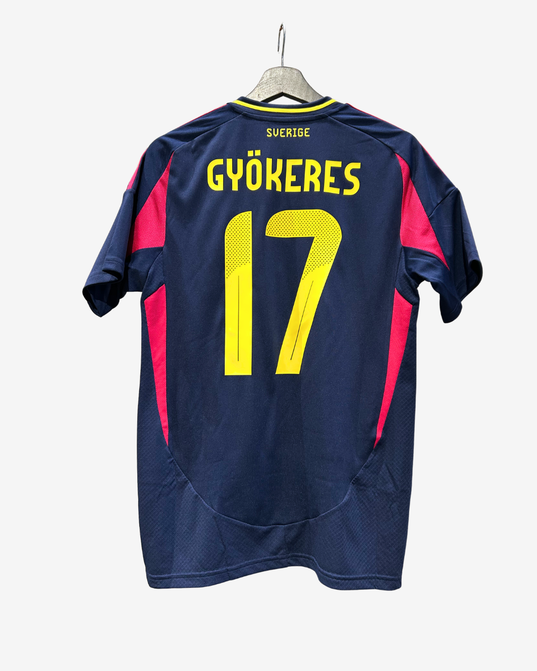 Back view of a navy blue soccer jersey hanging on a wooden hanger against a light gray background. The jersey features the name 'GYOKERES' and the number '17' in bright yellow, with pink side panels and yellow trim.
