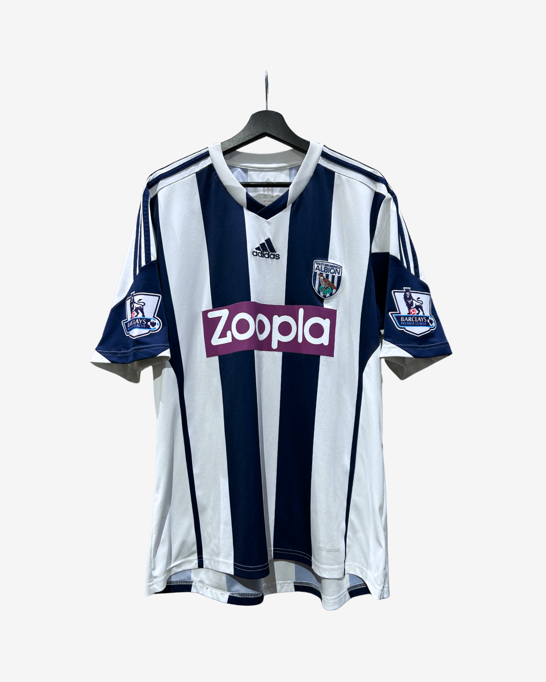 A vintage West Ham United home soccer jersey by Adidas, featuring navy and white vertical stripes with the purple 'Zoopla' sponsor logo on the chest, hanging on a black hanger against a light gray background.