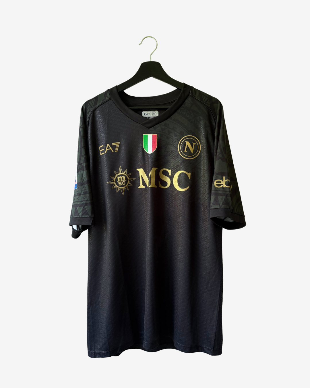 A black Napoli soccer jersey with gold and white sponsor logos, displayed on a black hanger against a light gray background.