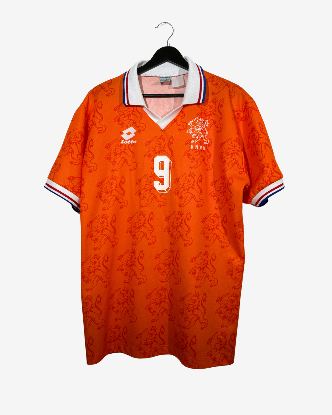 An orange short-sleeve soccer jersey with a subtle lion pattern, featuring the Dutch national team crest and the number 9 on the chest, hanging on a black hanger against a light gray background.