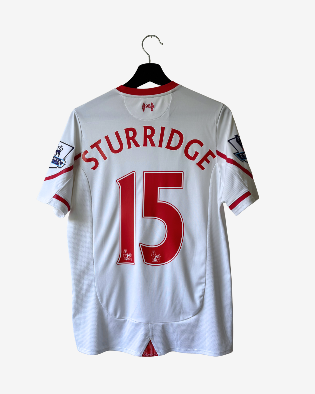 White Liverpool FC short-sleeve soccer jersey with 'STURRIDGE' and number 15 in red on the back, hanging on a black hanger against a light gray background.