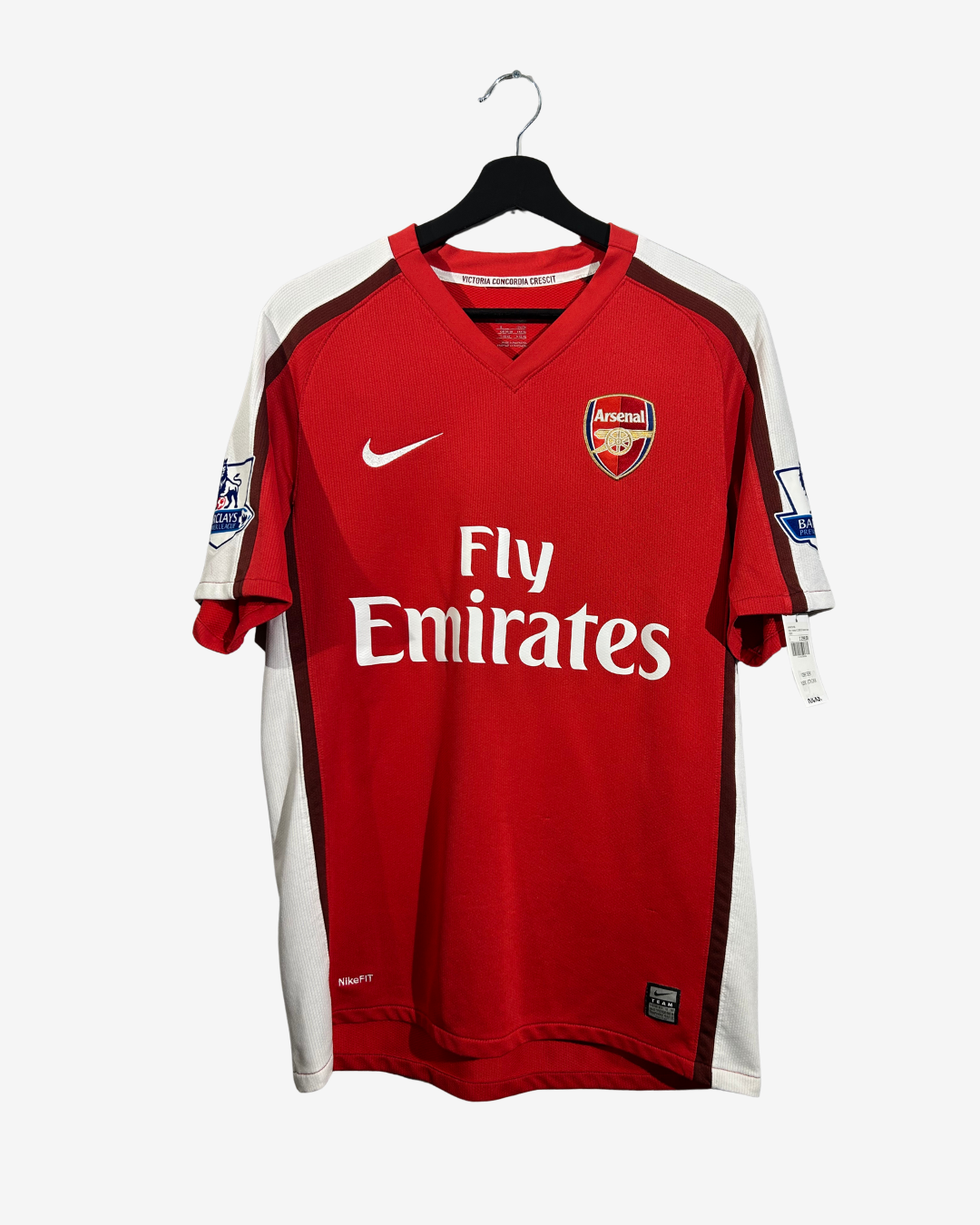 A red and white Arsenal football jersey with 'Fly Emirates' sponsor logo, displayed on a black hanger against a light gray background.