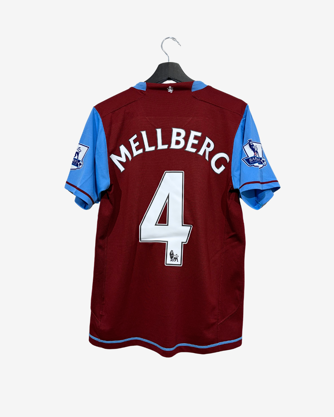 A maroon and blue Aston Villa football jersey shown from the back, hanging on a black hanger against a light gray background. The back features the name 'MELLBERG' in white lettering above a large white number '4'.