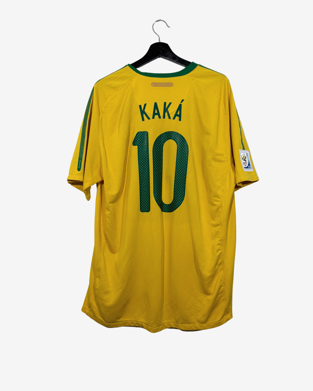 A yellow Brazil soccer jersey with 'KAKÁ' and the number '10' printed in green on the back, hanging on a black hanger against a light gray background.