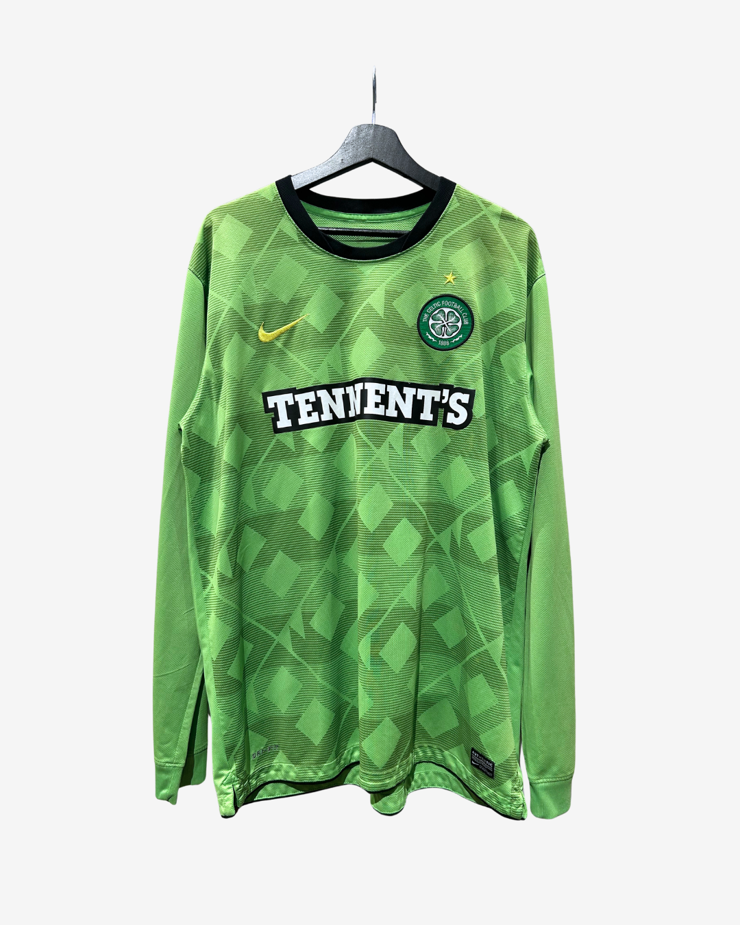 A green long-sleeve Celtic soccer jersey with a geometric pattern, featuring the Celtic crest, a yellow Nike swoosh, and 'TENIENT'S' sponsor text across the chest, hanging on a black hanger against a light gray background.