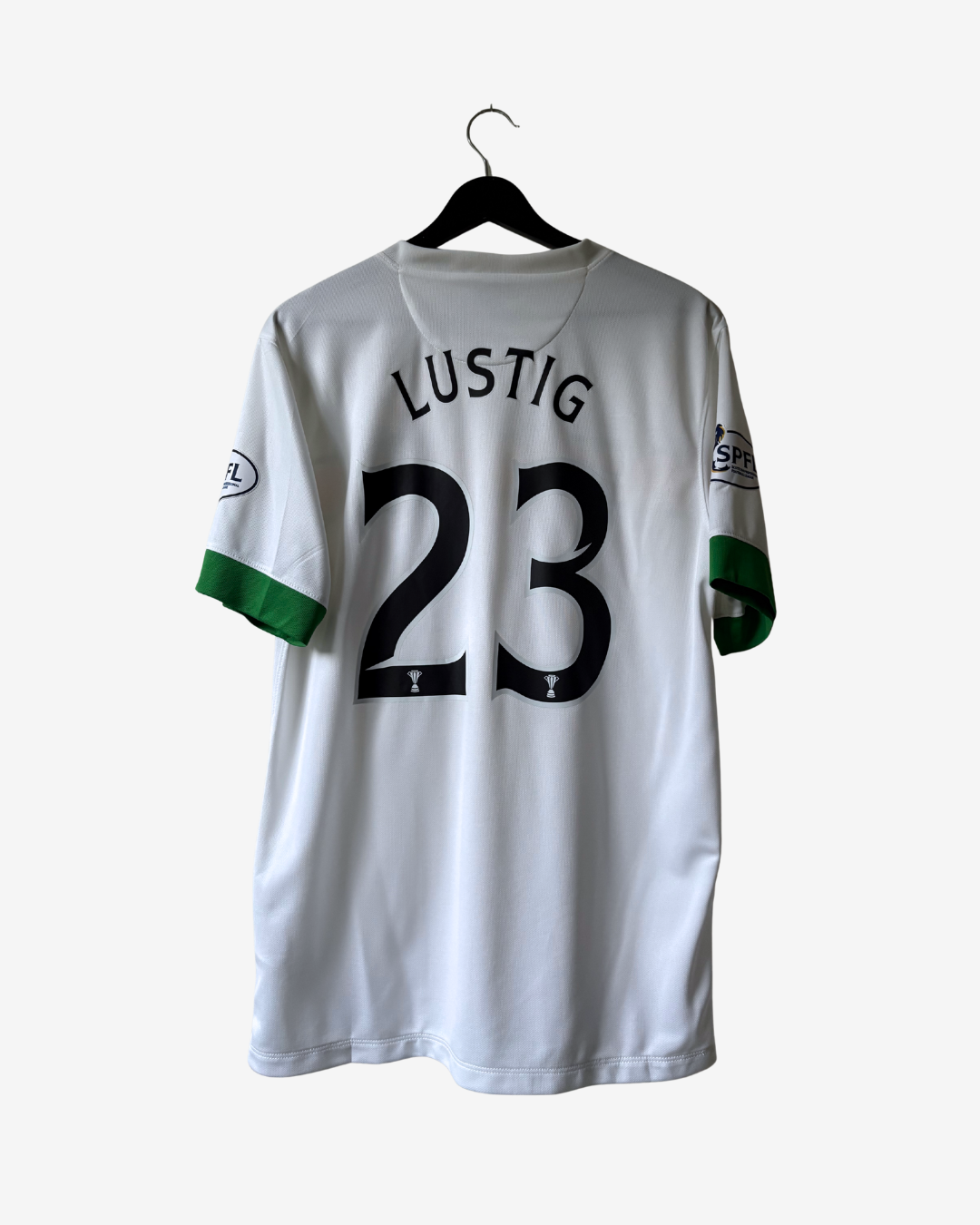 A white sports jersey with 'LUSTIG' and the number '23' printed in black on the back, featuring green sleeve accents, hanging on a black hanger against a light gray background.