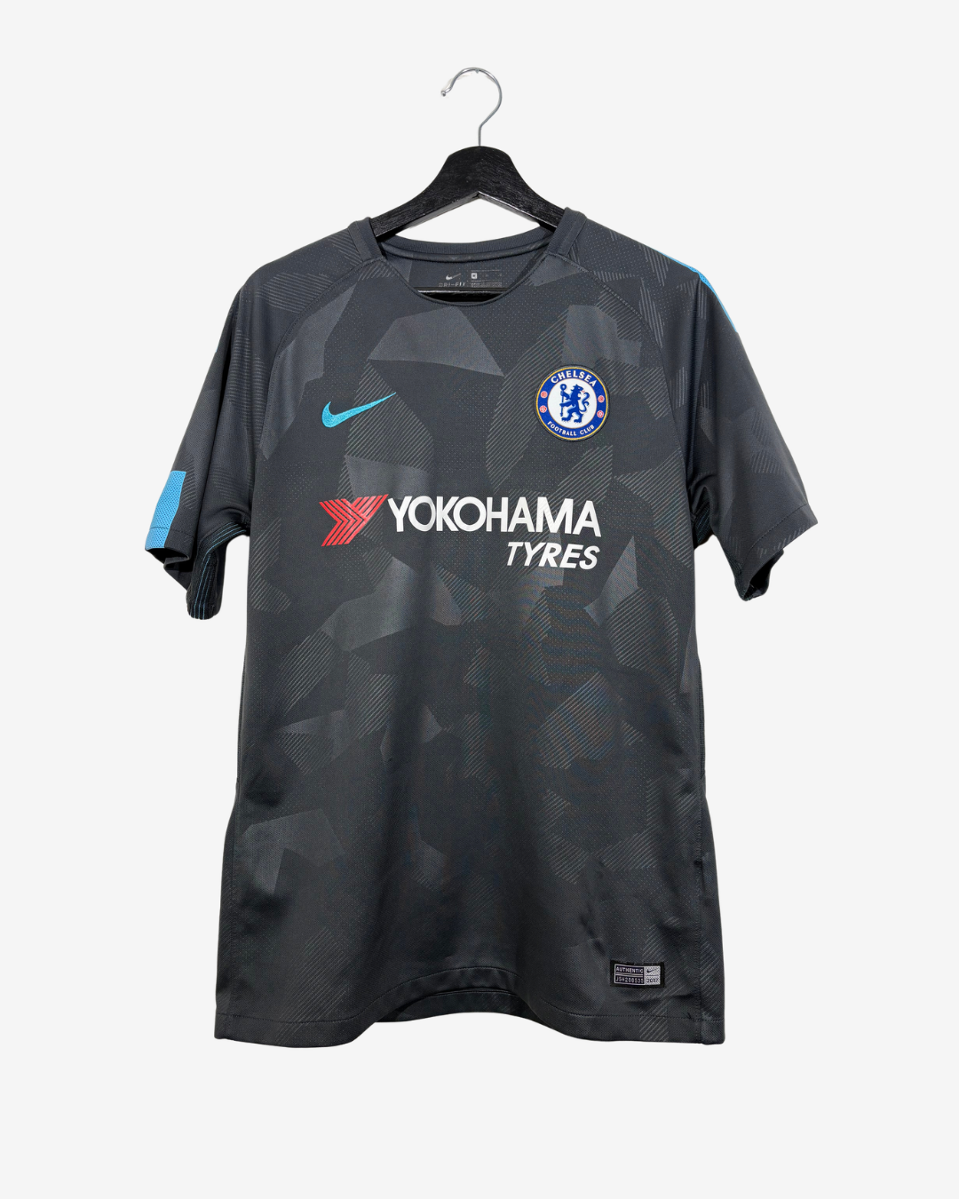 A dark gray Chelsea FC soccer jersey with a geometric pattern, featuring the Nike swoosh, Chelsea crest, and Yokohama Tyres sponsor logo, hanging on a black hanger against a light gray background.