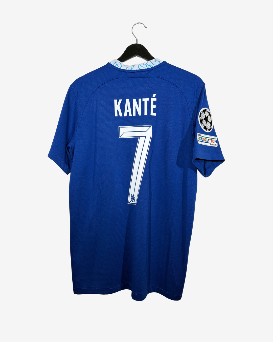 A royal blue Chelsea soccer jersey with 'KANTÉ' and the number '7' printed on the back, hanging on a black hanger against a light gray background.