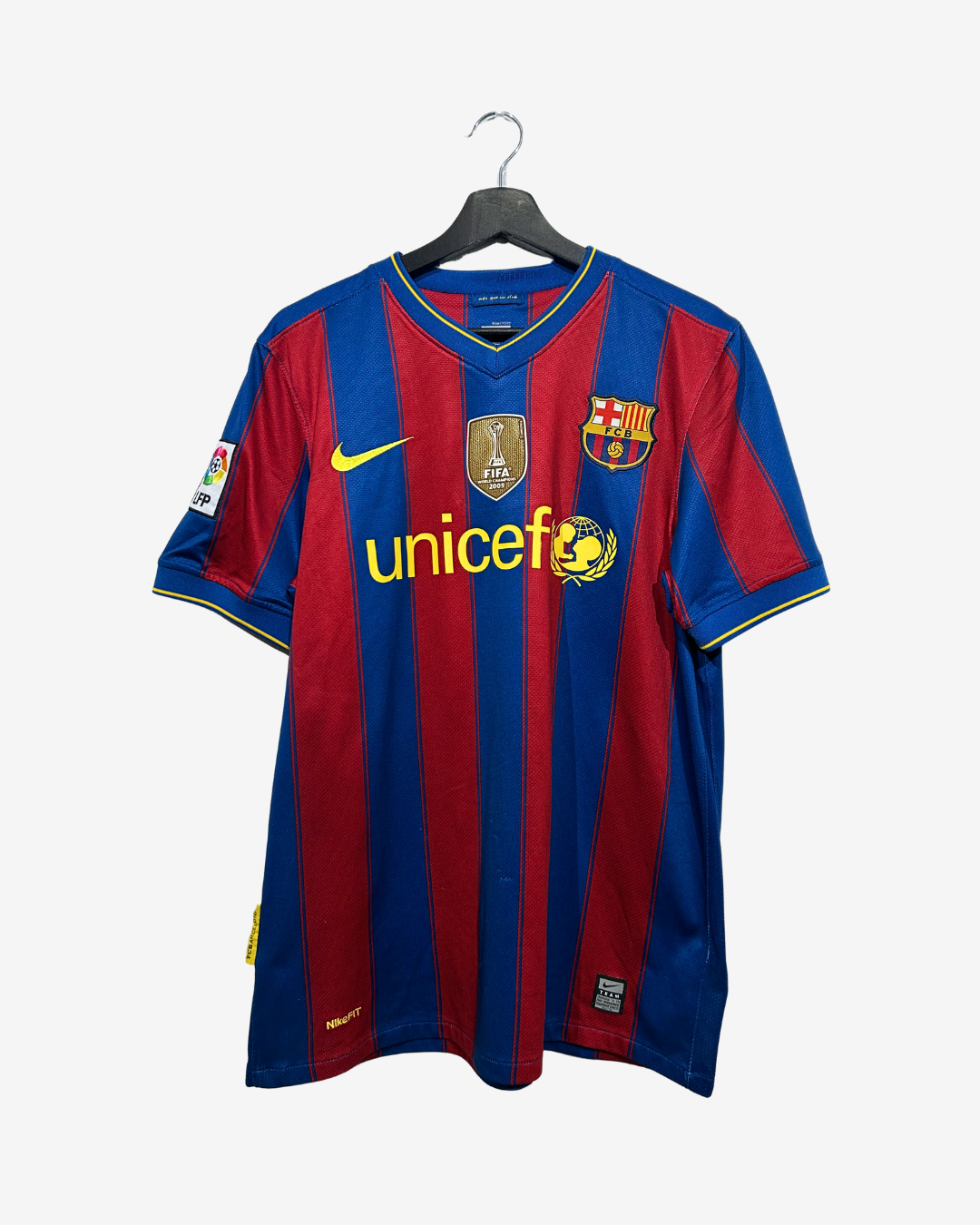 A vintage FC Barcelona home soccer jersey with red and blue vertical stripes, featuring the yellow Nike swoosh, Unicef sponsor logo, and FC Barcelona crest, hanging on a black hanger against a light gray background.