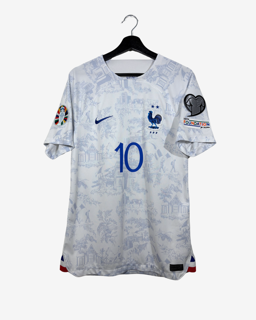A white and light blue patterned France national football team jersey with the number 10 on the front, hanging on a black hanger against a light gray background. It features the Nike swoosh, the French rooster crest, and various patch badges on the sleeves.