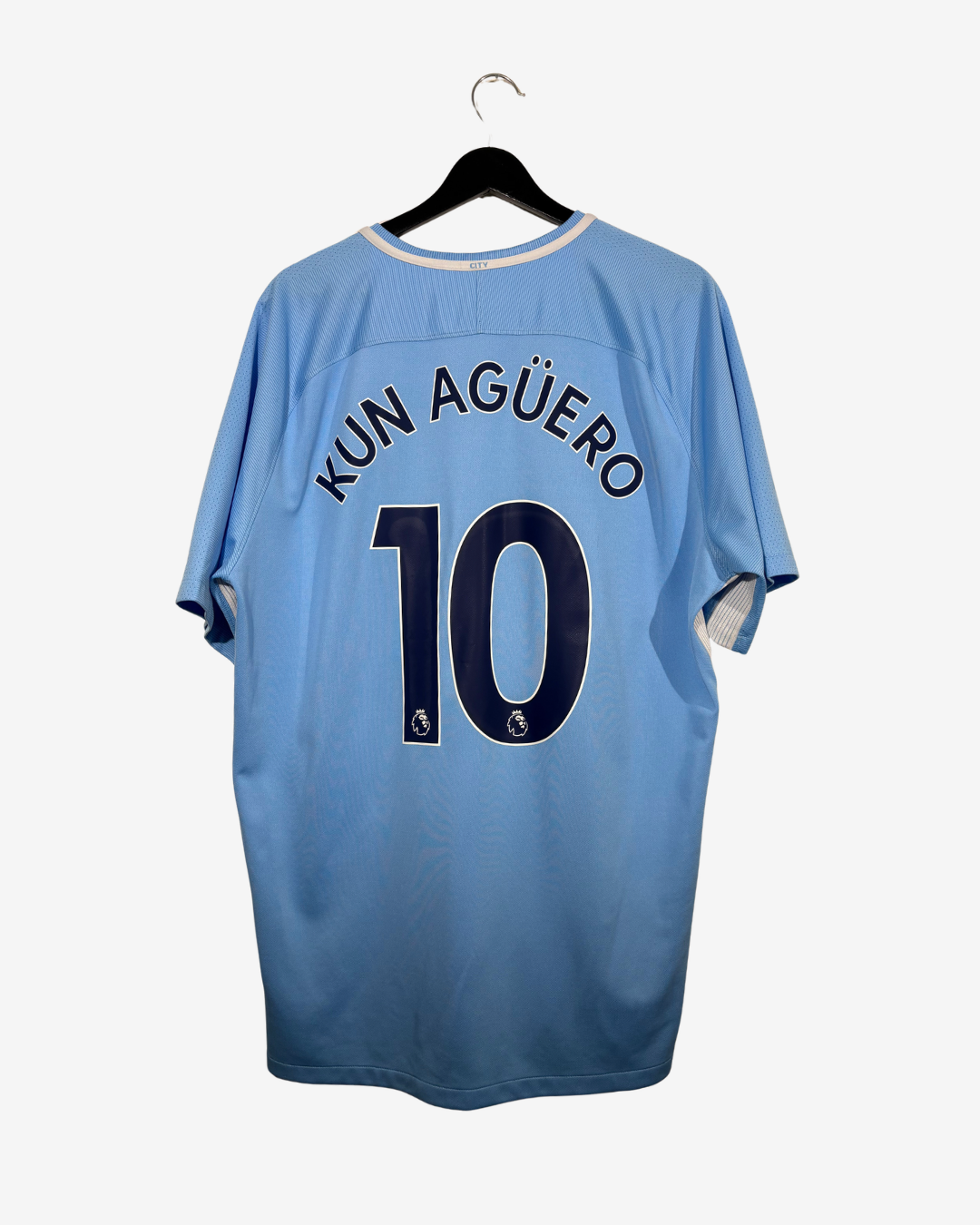 A light blue soccer jersey hanging on a black hanger against a light gray background. The back of the shirt features the name 'KUN AGÜERO' and the number '10' in dark navy blue with white outlines.