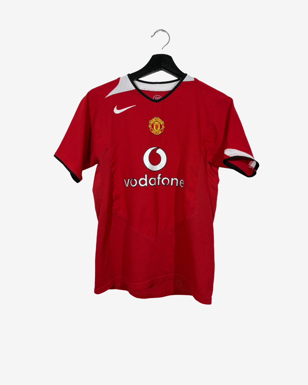 A red Manchester United short-sleeve soccer jersey by Nike, featuring the white Vodafone sponsor logo and the club crest, hanging on a black hanger against a light gray background.