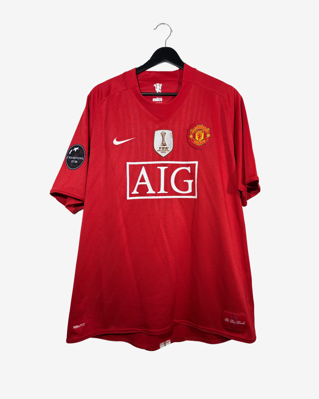 A red Manchester United soccer jersey by Nike, featuring the AIG sponsor logo, displayed on a black hanger against a light gray background.