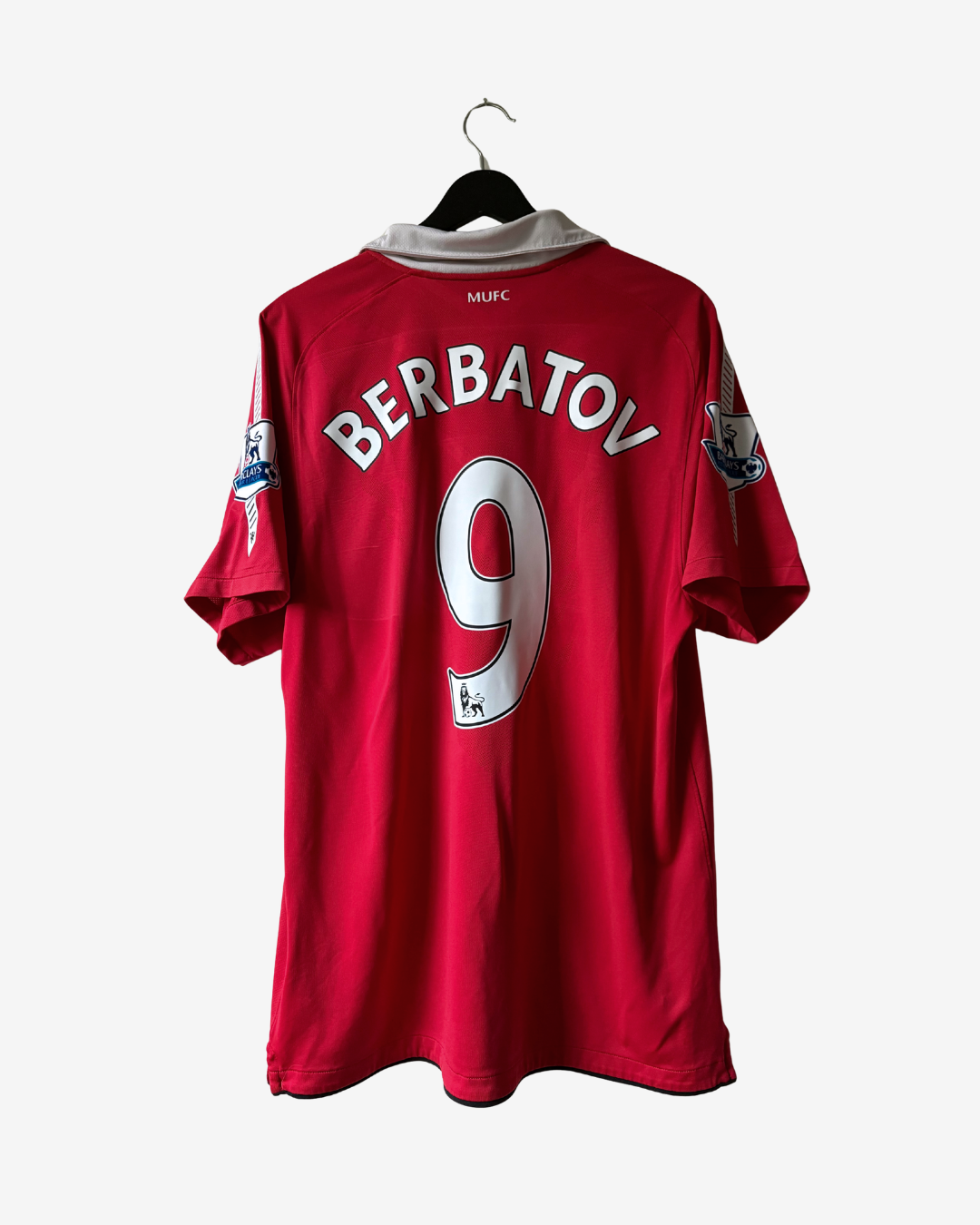 A red Manchester United football jersey with 'BERBATOV' and the number 9 printed on the back, hanging on a black hanger against a light gray background.
