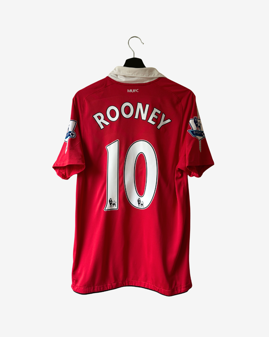 A red Manchester United short-sleeve soccer jersey with 'ROONEY 10' printed on the back, hanging on a black hanger against a light gray background.