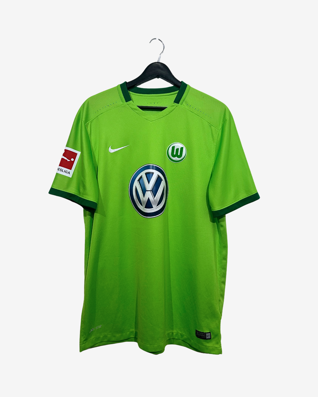 A bright green VfL Wolfsburg soccer jersey by Nike, hanging on a black hanger against a light gray background. The jersey features the Volkswagen logo on the center chest, the VfL Wolfsburg crest on the right chest, and a Bundesliga patch on the left sleeve.
