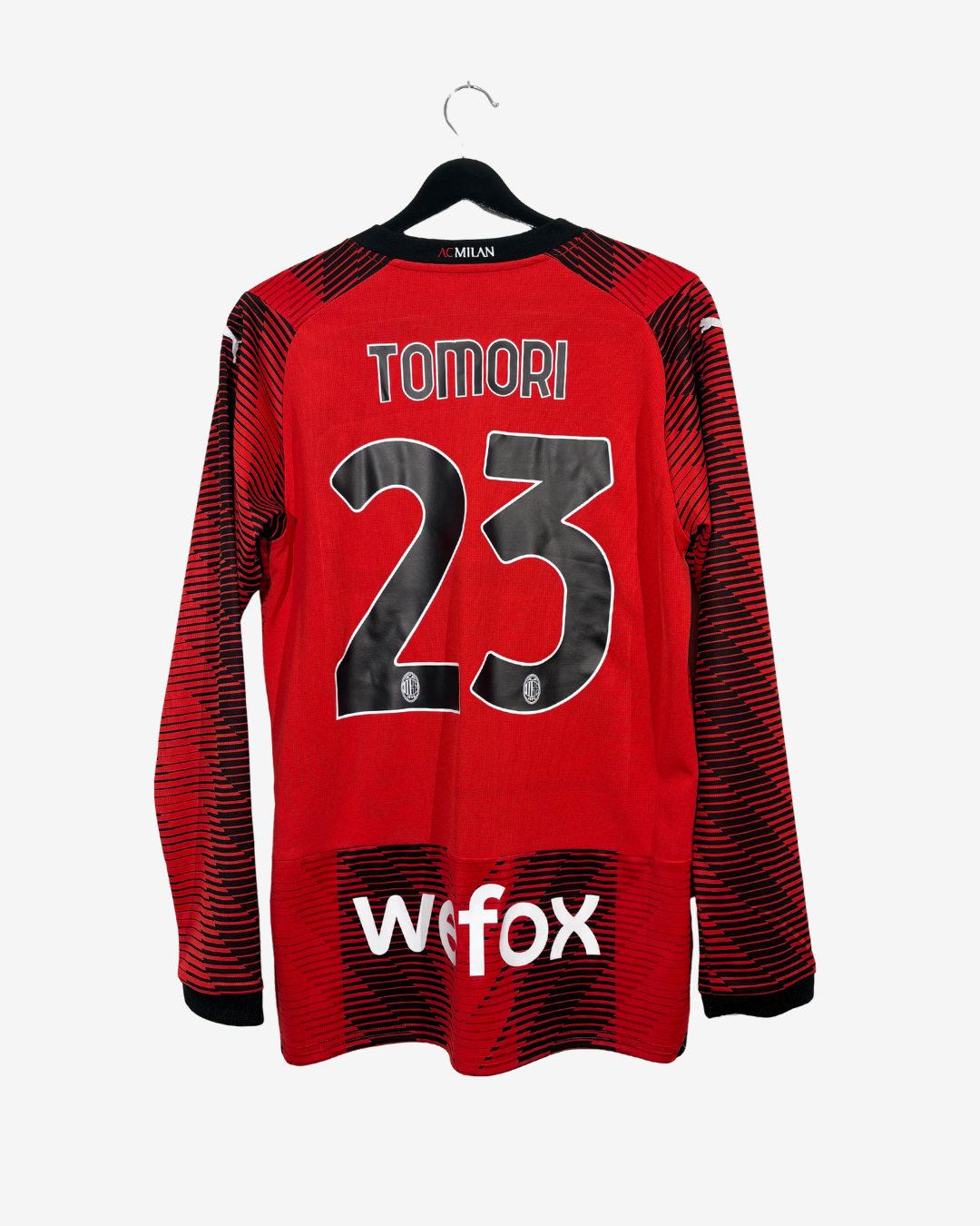 A red long-sleeve soccer jersey with black patterned sleeves and hem, featuring the name TOMORI and number 23 on the back, with a white wifo sponsor logo near the bottom. The jersey is shown hanging on a black hanger against a light gray background.