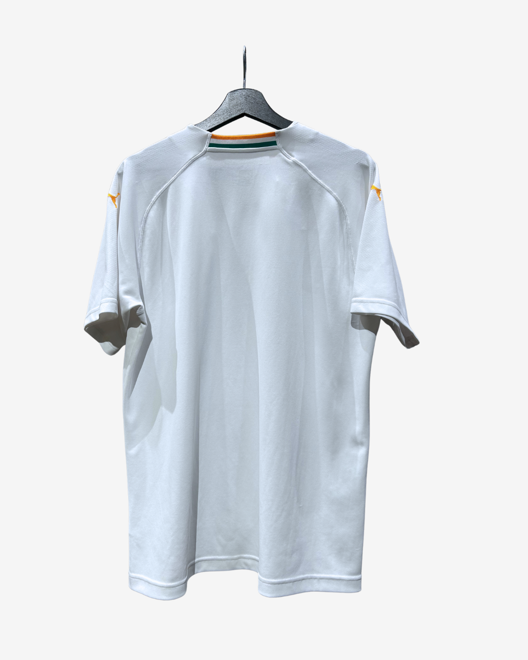 A white short-sleeve athletic jersey hanging on a black hanger against a light gray background. The back of the shirt features raglan sleeves, a crew neck with green and orange stripes, and small yellow logo accents on the shoulders.