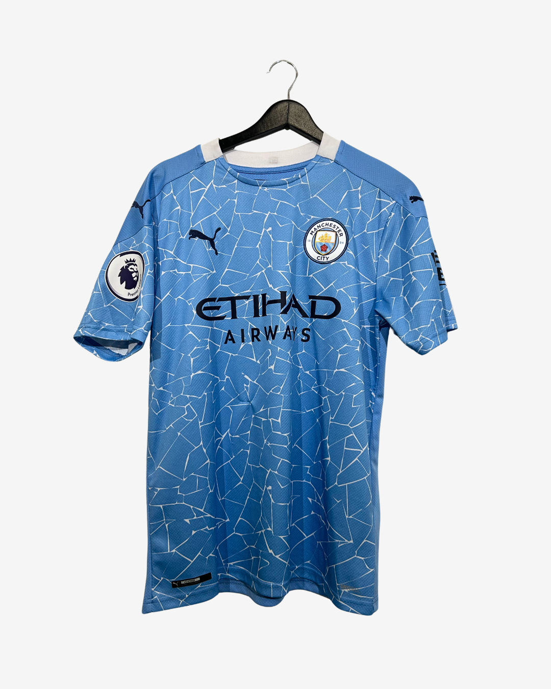 A light blue Puma Manchester City home soccer jersey with a white abstract line pattern, featuring the Etihad Airways sponsor logo, displayed on a black hanger against a light gray background.