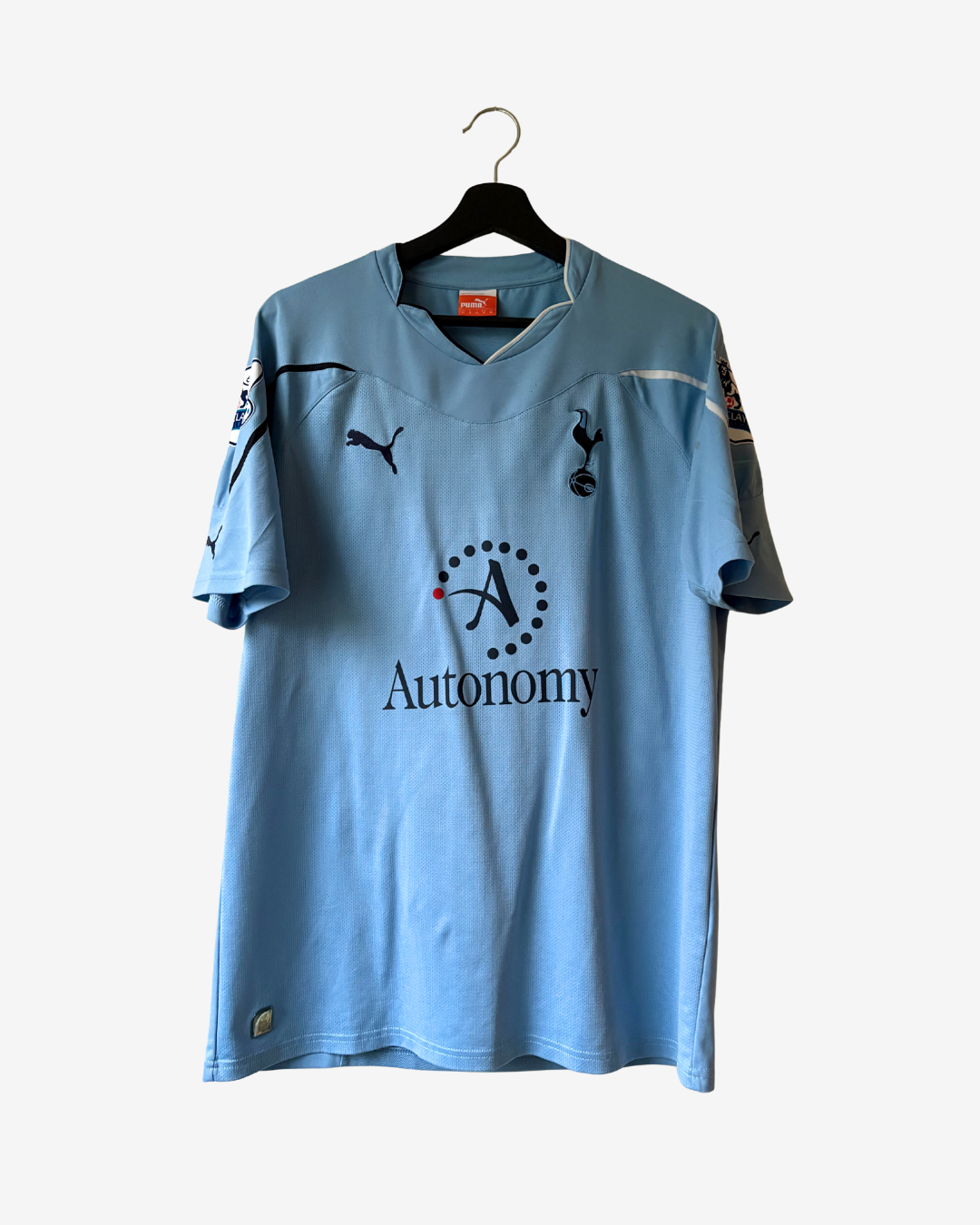 A light blue Tottenham Hotspur football jersey by Puma, featuring the 'Autonomy' sponsor logo on the front, hanging on a black hanger against a light gray background.