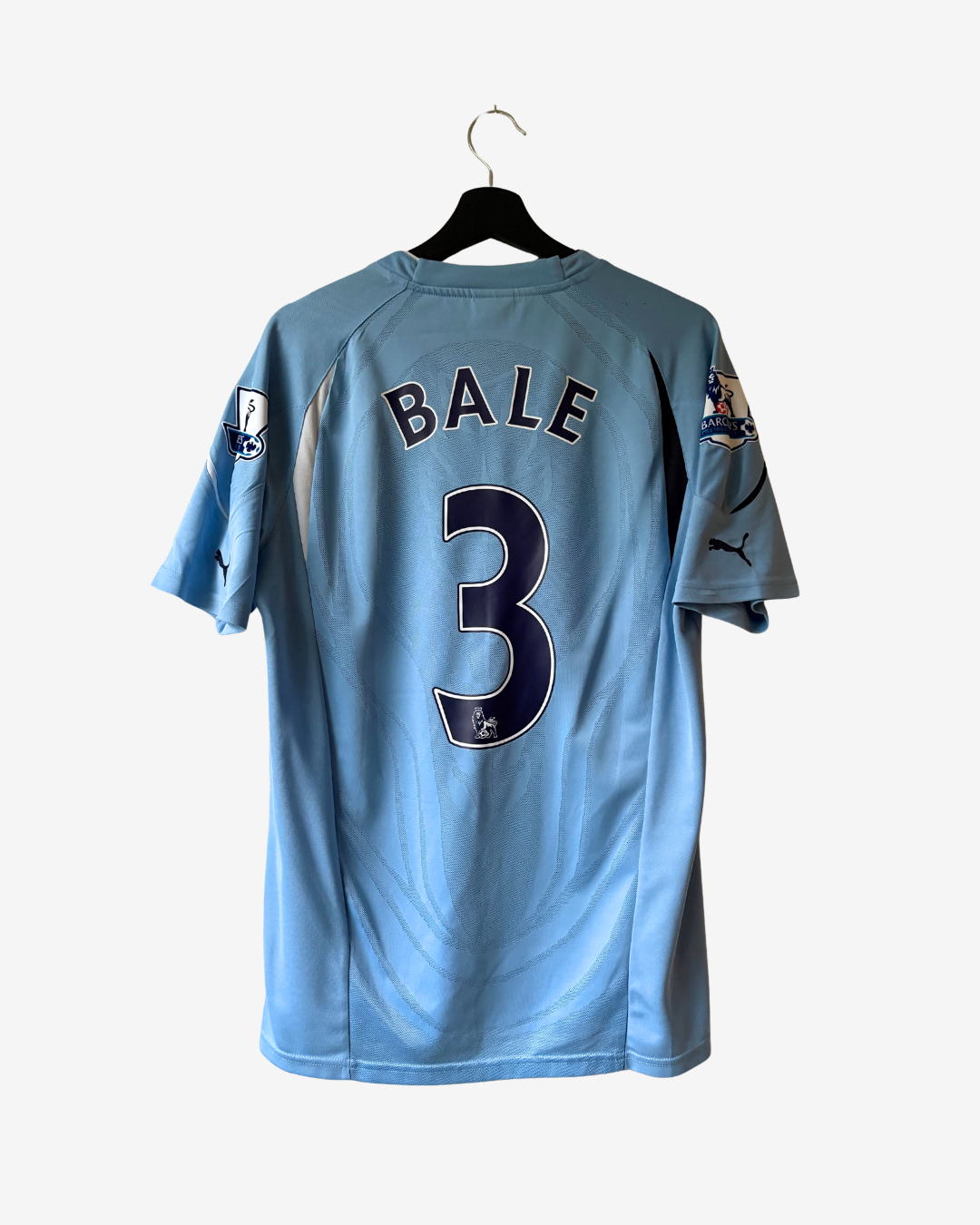 A light blue Tottenham soccer jersey with 'BALE' and the number '3' printed on the back, hanging on a black hanger against a light gray background.