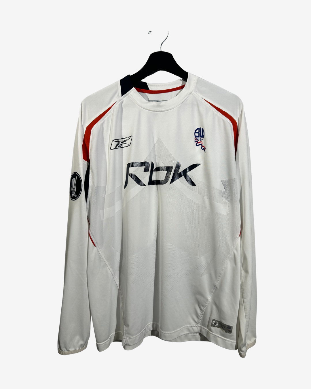 A white long-sleeve athletic jersey with black and red accents, featuring 'RBK' printed across the chest, hanging on a black hanger against a light gray background.