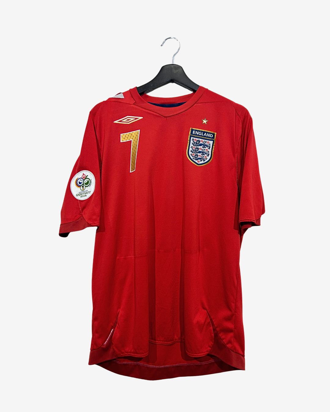 A red England national football team jersey with the number 7 on the front, hanging on a black hanger against a light gray background. It features the Umbro logo on the right chest, the England crest on the left chest, and a Premier League patch on the sleeve.
